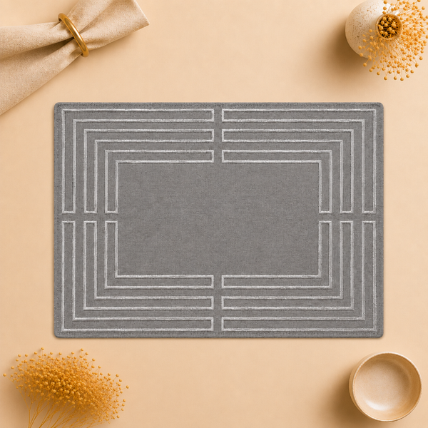 A rectangular gray placemat with a white geometric border pattern, styled in a flat-lay on a beige background with decorative dried flowers and a napkin.