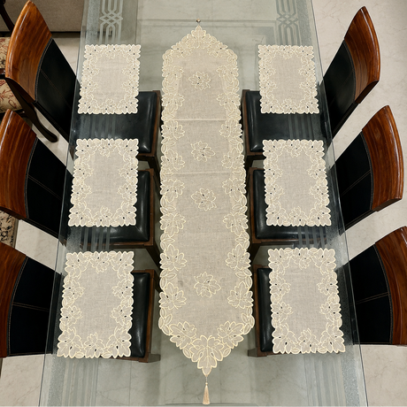 An ivory lace table runner and matching placemats set on a glass dining table surrounded by wooden chairs.