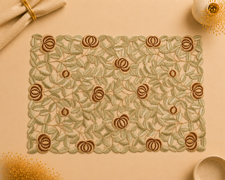A rectangular embroidered placemat with a repeating floral and leaf pattern in muted green and brown, styled on a warm beige surface with decorative props.