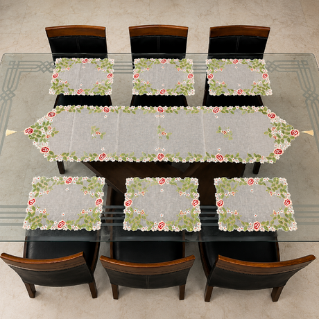A dining table set with a floral table runner and matching rectangular placemats, shown from above on a glass-top dining table with six chairs.