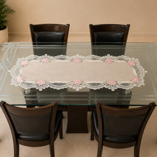 A rectangular table runner with a beige linen center and white lace floral borders, displayed on a glass-top dining table with four dark chairs.