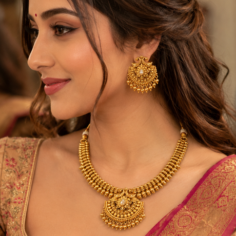 Woman wearing gold jewelry including earrings and a necklace, with a blurred background.