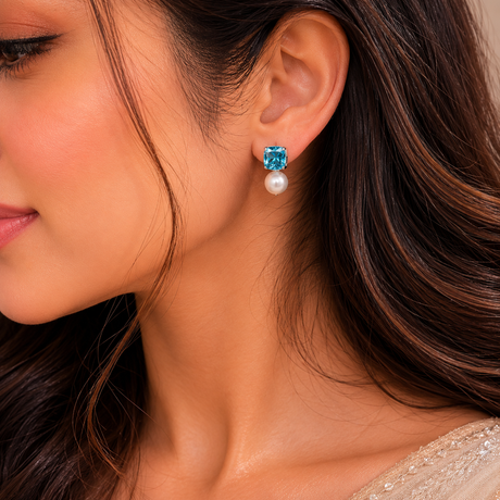 Close-up of a woman wearing blue topaz and pearl earrings.