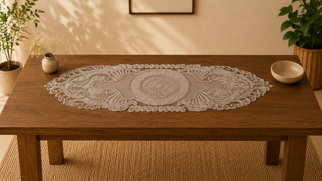 Decorative lace table runner on a wooden table with plants and a bowl in a warm-toned room.