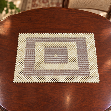 A rectangular woven placemat with concentric square patterns in cream and taupe, displayed on a round dark wood dining table.