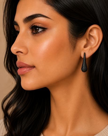 Close-up of a woman wearing a black teardrop earring with a neutral background