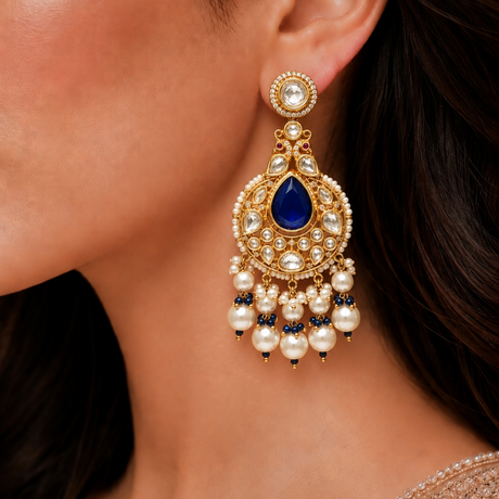 Close-up of a woman wearing a gold earring with blue gemstone and pearl details.