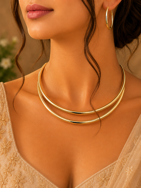 Close-up of a woman wearing a gold necklace and hoop earrings with a blurred background.