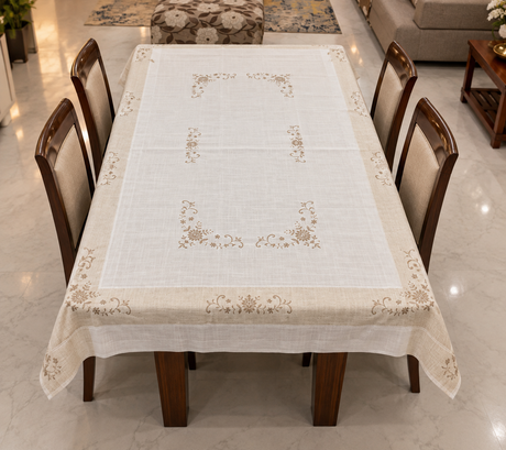 A square white linen tablecloth with a beige border featuring delicate floral and scroll embroidery, laid flat.