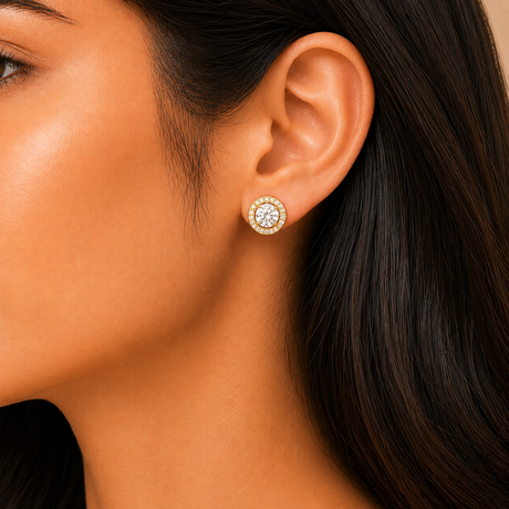 Close-up of a woman wearing gold earrings with a clear gemstone.