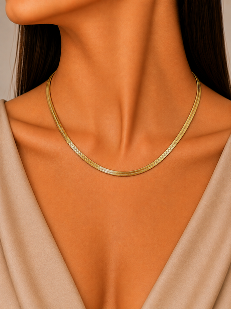 Gold necklace on a person wearing a beige top against a neutral background