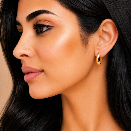 Close-up of a woman wearing gold hoop earrings with a neutral background