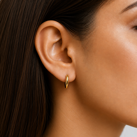 Close-up of a person wearing a gold hoop earring with dark hair and skin.