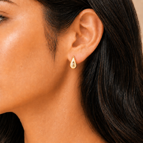 Close-up of a person wearing a gold earring with dark hair and skin.