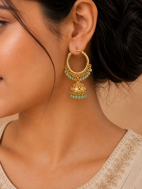 Close-up of a gold earring with green beads worn by a person.