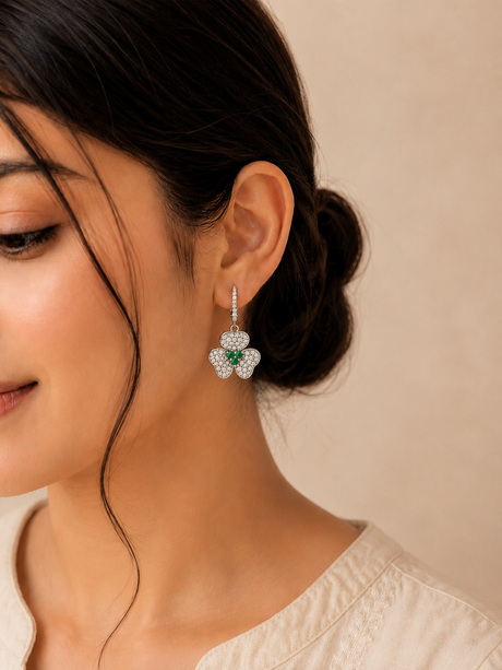 Close-up of a woman wearing emerald and diamond earrings against a beige background