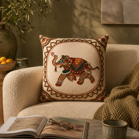 Decorative pillow with an embroidered elephant design on a beige armchair.