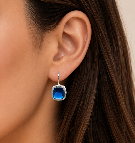 Close-up of an ear wearing a blue gemstone earring with a blurred background