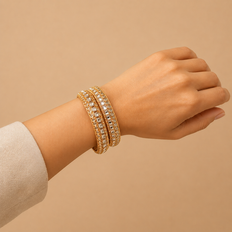 Hand wearing two gold bracelets on a beige background