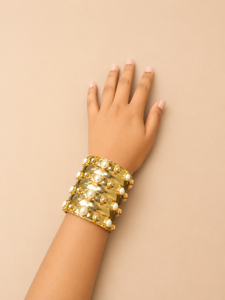 Gold bracelet on a hand against a beige background