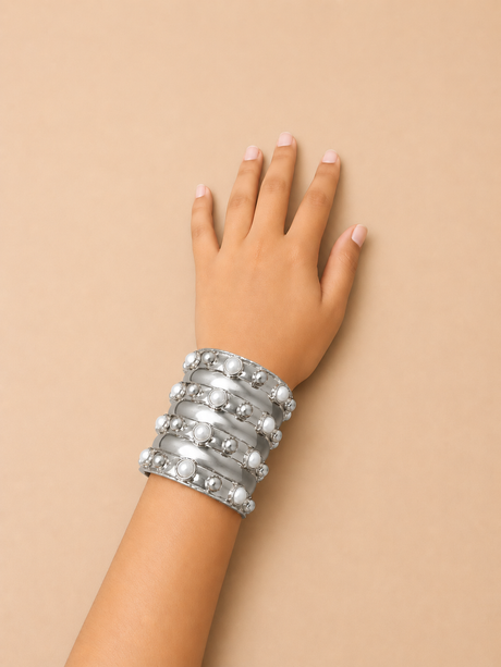 Hand wearing multiple silver bracelets on a beige background