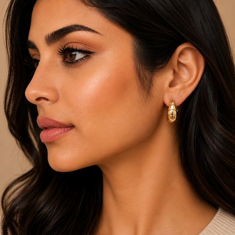 Close-up of a woman wearing gold earrings with a neutral background