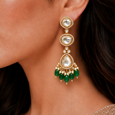 Close-up of a woman wearing a gold earring with green gemstones.