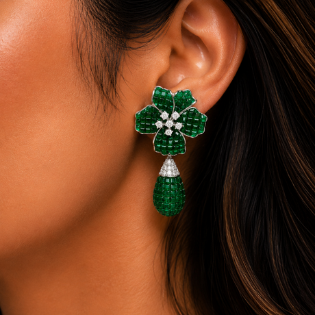 Close-up of a person wearing a green floral earring with a teardrop-shaped gem.