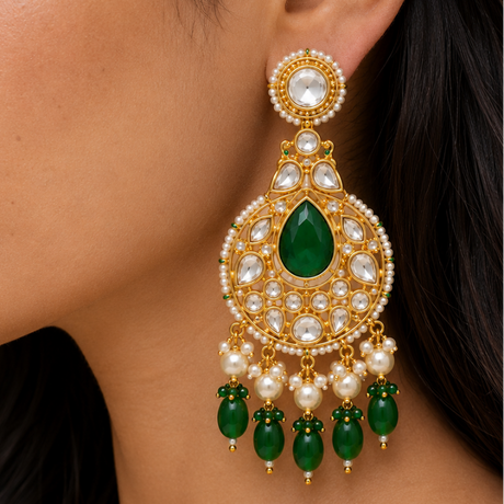 Close-up of a woman wearing a gold earring with green gemstones and pearls.