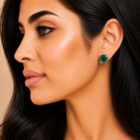 Close-up of a woman wearing green gemstone earrings with a neutral background