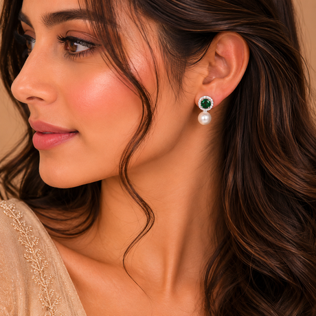Close-up of a woman wearing green gemstone and pearl earrings against a neutral background