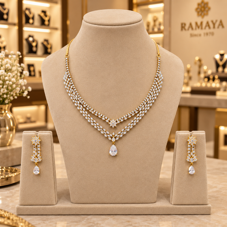A gold and crystal jewelry set displayed on a beige mannequin bust in a luxury jewelry store. The set includes a three-row layered necklace with a teardrop pendant, matching drop earrings, and a small box.