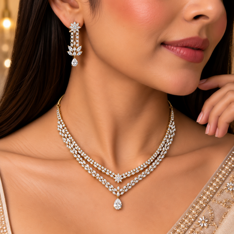 A close-up lifestyle shot of a woman wearing a gold double-row diamond necklace with a teardrop pendant, matching diamond drop earrings, and a beige embellished sari.