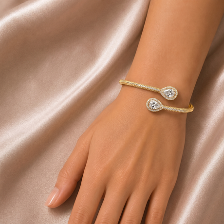 Gold bracelet with a clear gemstone on a hand against a beige fabric background