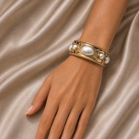 Gold bracelet with pearls on a hand against a beige fabric background