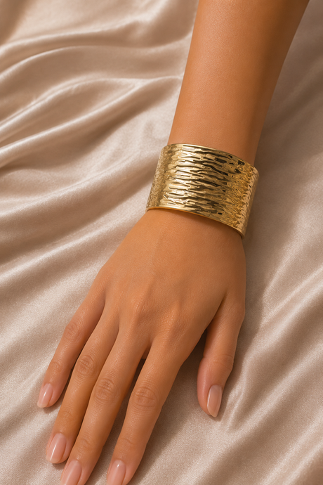 Gold textured bracelet on a hand against a beige fabric background