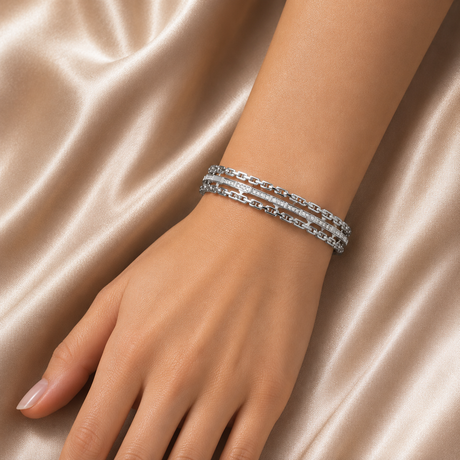 Hand wearing a stack of silver bracelets on a satin background