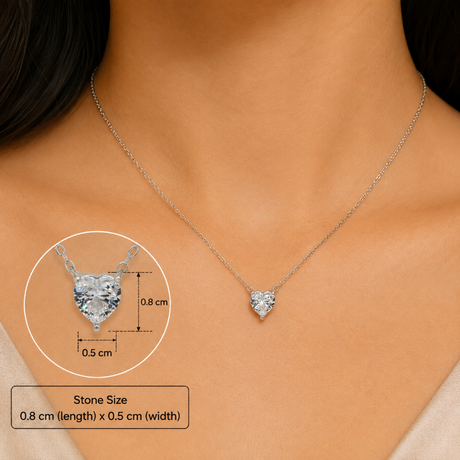 A silver heart-shaped pendant necklace with a clear heart-shaped gemstone is shown on a model's neck. The image includes a circular inset showing the pendant in detail with dimensions (0.