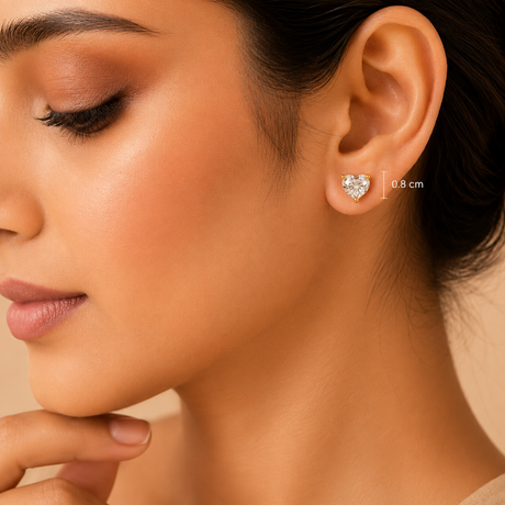 Close-up of a woman's ear wearing a small heart-shaped silver stud earring with a clear gemstone. A small '0.