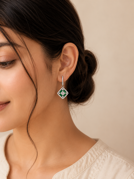 Woman wearing a pair of emerald green earrings with a beige background
