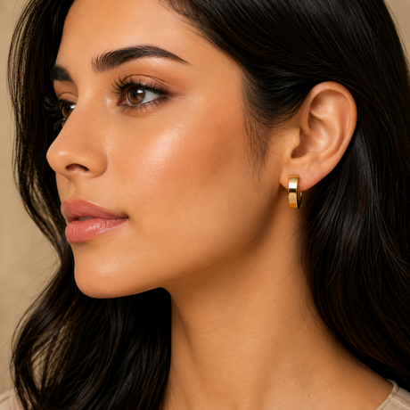 Close-up of a woman wearing a gold hoop earring against a neutral background
