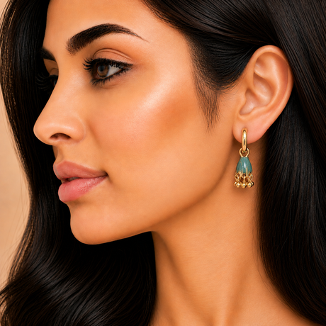 Close-up of a woman wearing a gold earring with a blue gemstone.