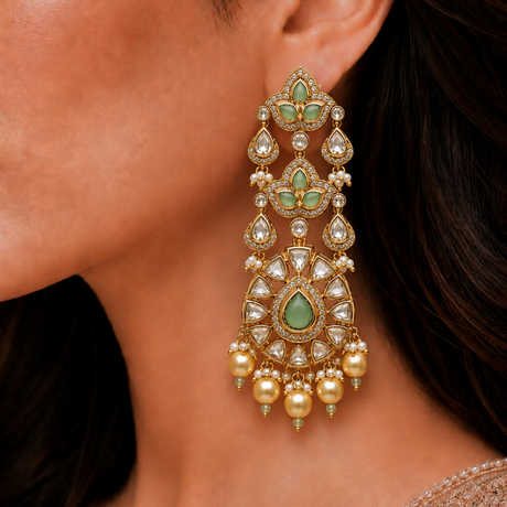 Close-up of a person wearing an ornate earring with green gemstones and gold accents.