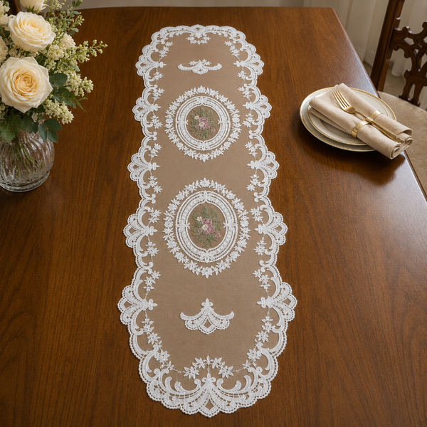 Decorative lace table runner on a wooden table with flowers and plates.