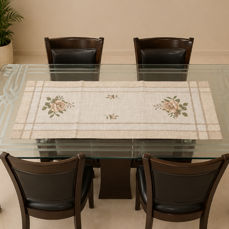 A rectangular glass-top dining table with four dark wooden chairs, featuring a beige woven table runner with floral embroidery down the center, set in a dining room.