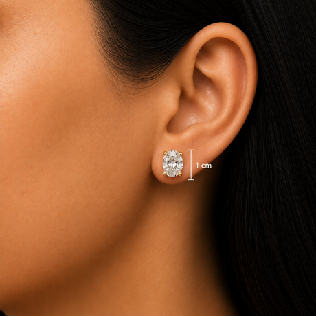 Close-up of a model's ear wearing a small oval stud earring, with a vertical measurement marker indicating the earring size is 1 cm.