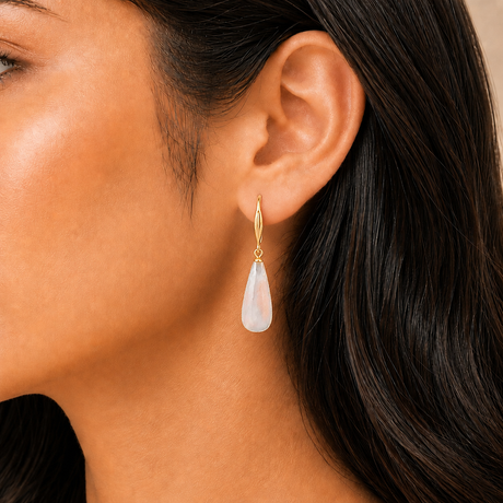 Close-up of a woman wearing a gold earring with a teardrop-shaped pearl.