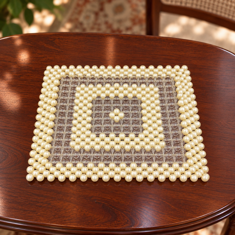 A square decorative placemat with concentric geometric patterns in cream and taupe, bordered by faux pearls, displayed on a dark wood table.