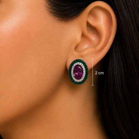 Close-up of a model's ear wearing an oval stud earring with a deep purple center stone, surrounded by a halo of small clear stones and a dark green outer border. A vertical measurement marker indicates the earring's height is 2 cm.