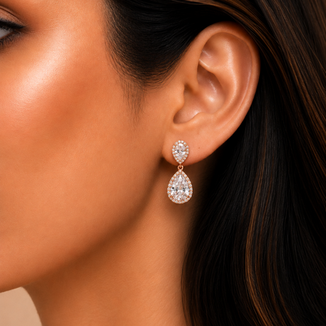 Close-up of a woman wearing teardrop-shaped diamond earrings with a neutral background